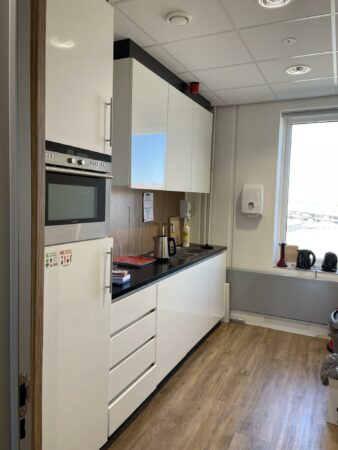Moderne kantoorkeuken met witte kasten, ingebouwde apparaten en uitzicht op de Johan Cruijff Boulevard.